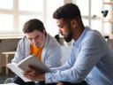 A young man read a book with another young man. These efforts will be helped by nonprofit CRM tools.