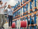 Two warehouse workers, a man and a woman, look over many large spools of fiber. / fiber to the home