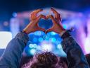 Photo of a woman at a concert at night, making a heart symbol with her hands / brand experience