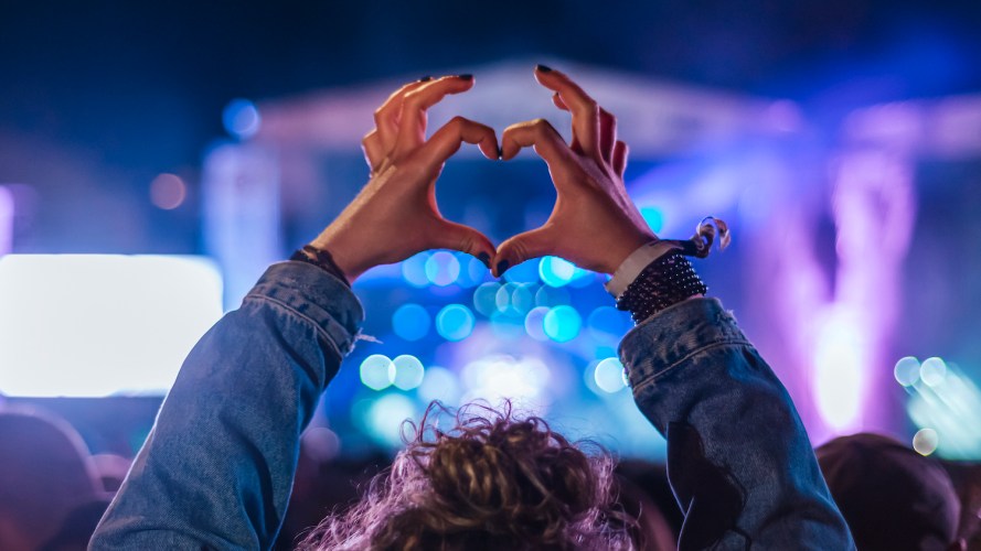 Photo of a woman at a concert at night, making a heart symbol with her hands / brand experience
