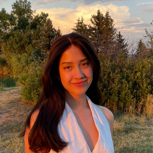 Jade Franson smiles at the camera. There's a sunset glow on her face and trees in the background.