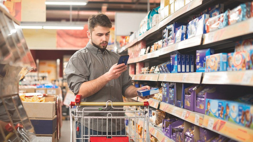 A grocery shopper uses their smartphone to compare the price of items online: retail pricing