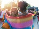 Rear view image of young couple walking with the pride event, hugging and waving pride flags during transgender awareness week