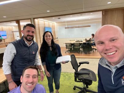 Hanna and three of her colleagues are smiling and posing for a casual group photo in a modern office.