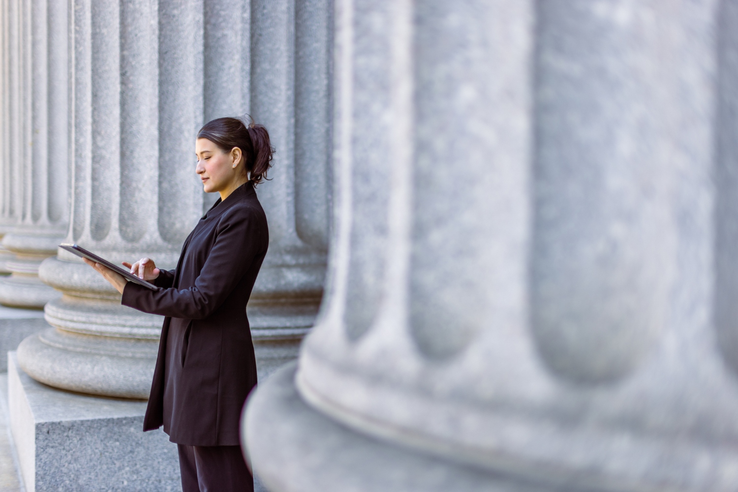 Hispanic female lawyer in front of a court house examining government data and analytics on a tablet.
