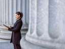 Hispanic female lawyer in front of a court house examining government data and analytics on a tablet.