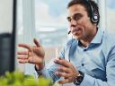 A male contact center agent in a headset and blue collared shirt uses a case management system to deliver excellent service