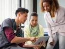 Male nurse working to improve the patient experience with two patients in an exam room.