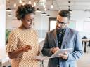 Photo of a man (holding a tablet) and a woman speaking in an office setting. / AI in B2B marketing