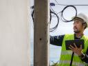 A telecom worker in a hard hat checking wires atop a utility poll.