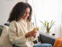 A smiling woman in a white sweater gets good customer service on her yellow mobile device from her couch