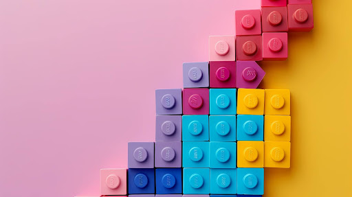 A colorful stack of large leggo blocks forming a triangle upwards on a pink background.