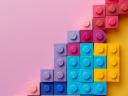 A colorful stack of large leggo blocks forming a triangle upwards on a pink background.