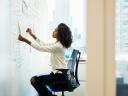 A woman entrepreneur sitting in a chair at a whiteboard arranging a project management system