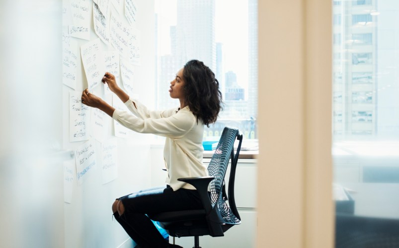 A woman entrepreneur sitting in a chair at a whiteboard arranging a project management system