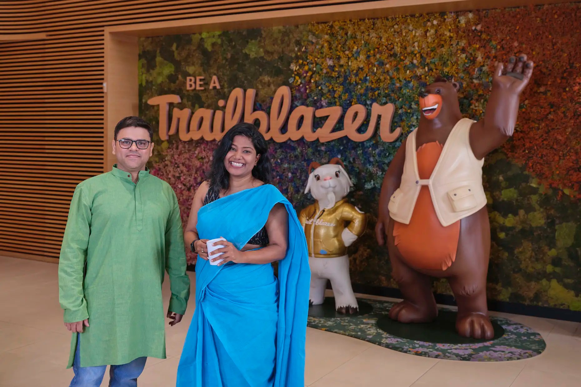 A man and a woman standing in front of Salesforce mascots Cody and Cloudy and a wall display saying "be a trailblazer"
