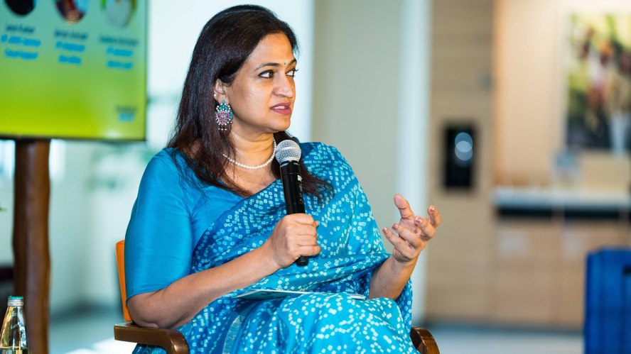 Photo of Sangeeta Giri Gundala sitting and holding a microphone, speaking to an audience.
