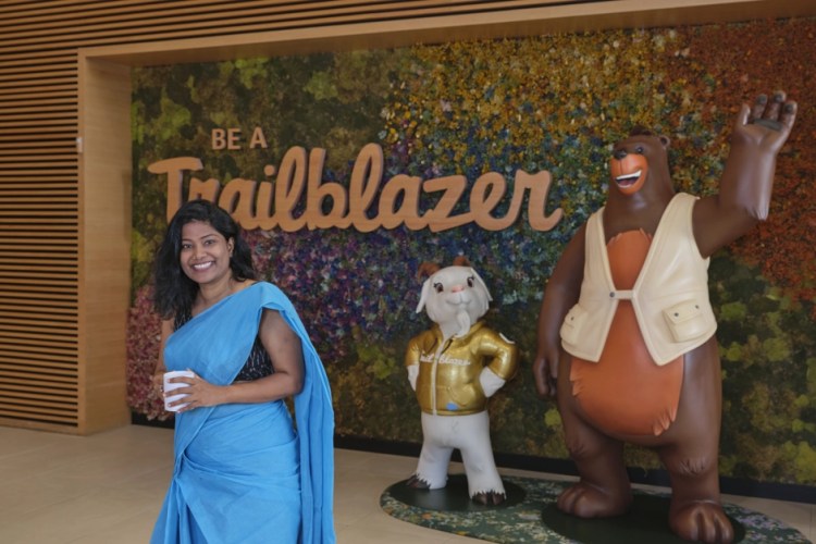A woman wearing Indian traditional clothes is samiling and posing next to Salesforce mascots and a sign that says: "Trailblazer".