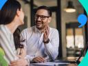 Sales people sitting at a table and smiling while asking SPIN selling questions. Background is blue with quote icon.