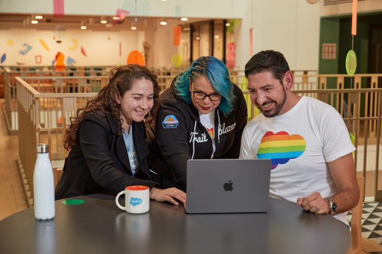 Three Salesforce employees smiling while looking at a computer