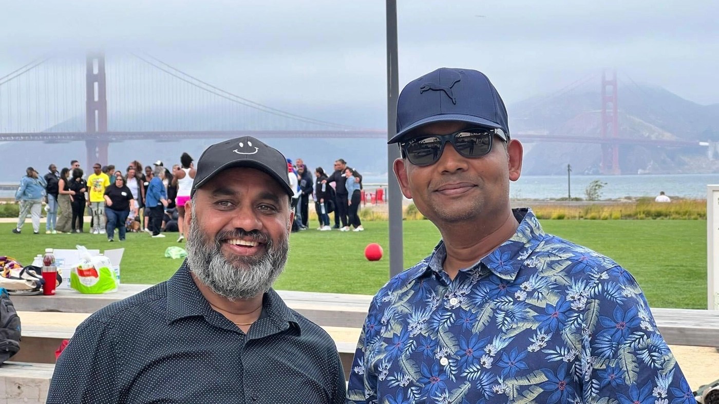 Two smiling men pose for a photo outdoors with the Golden Gate Bridge in the background.