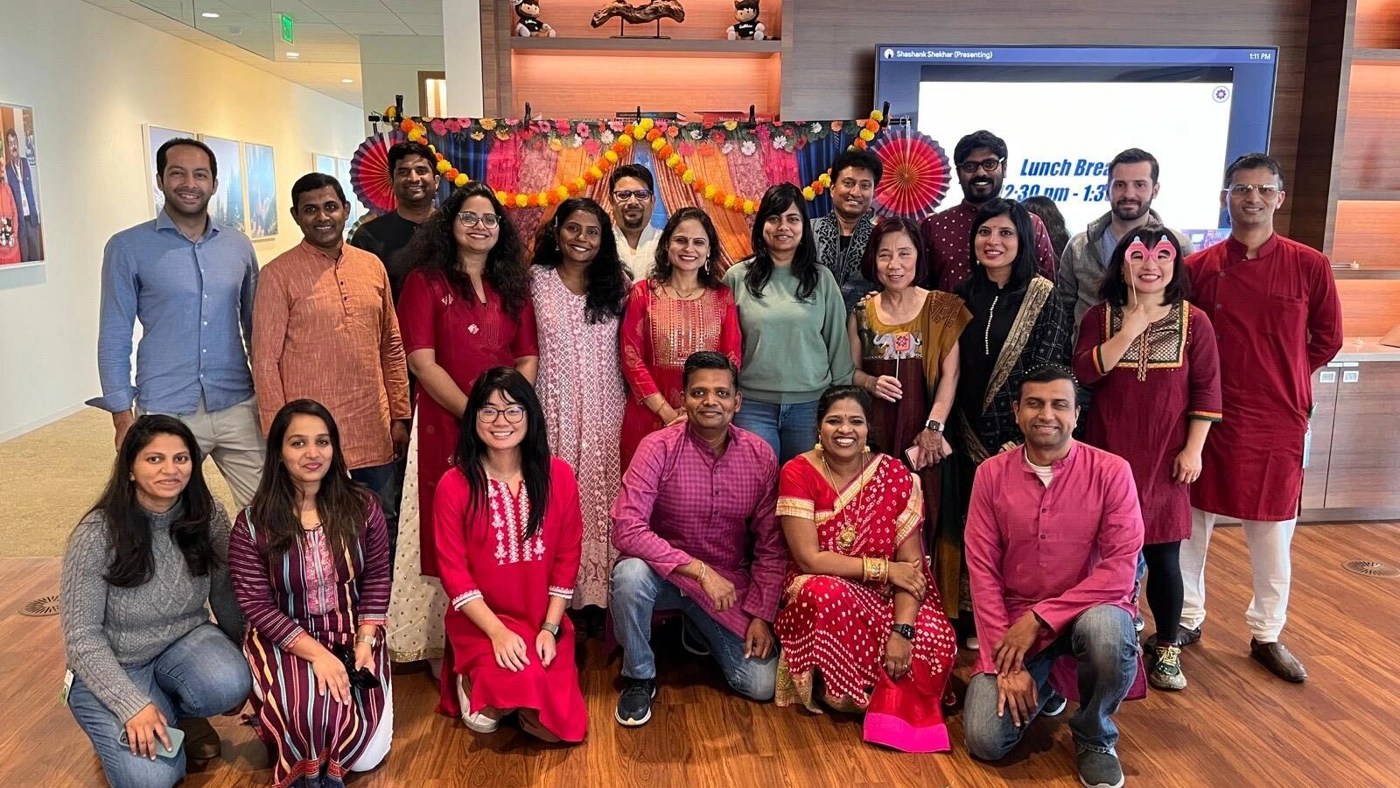 A group of coworkers dressed in traditional clothes poses together with festive decorations in the background.