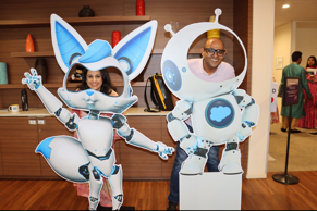 Two Salesforce employees pose playfully with cutouts of Salesforce mascots Astro and Codey at an indoor event.