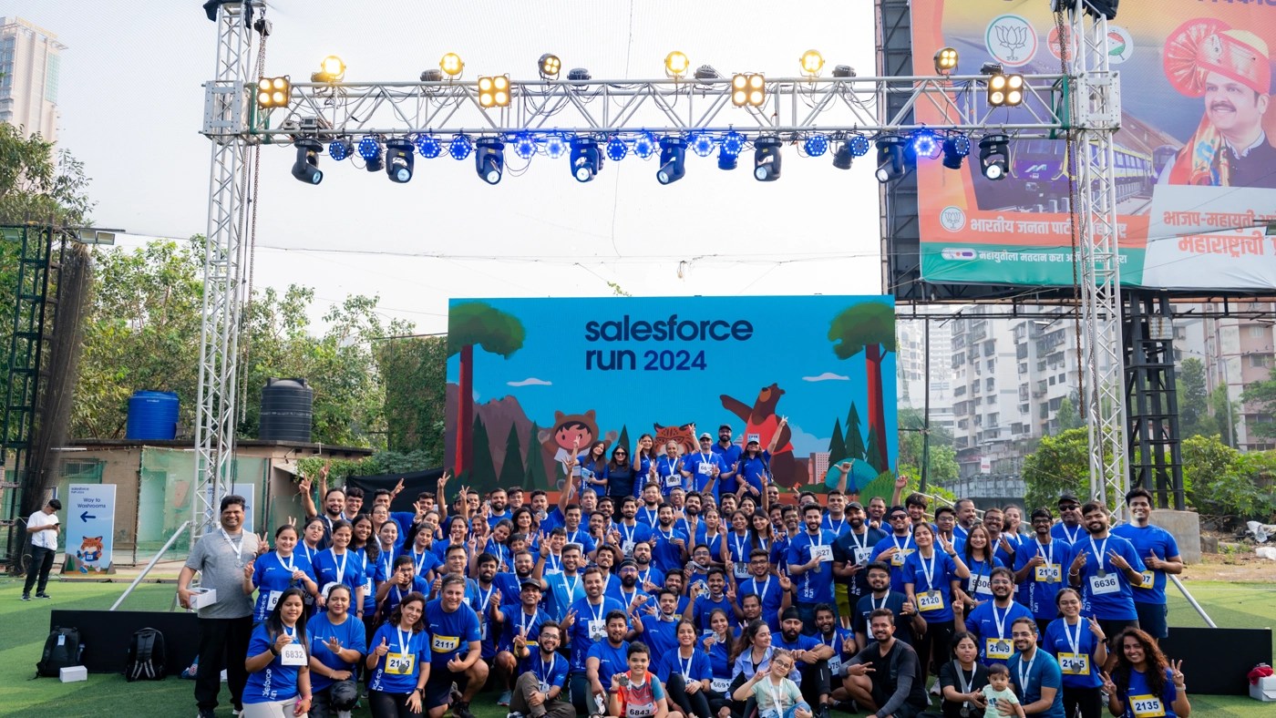Salesforce India employees who participated in the event Salesforce Run 2024 pose in front of a stage