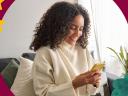 A smiling woman in a white sweater gets good customer service on her yellow mobile device from her couch