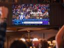Image of fans at a bar celebrating while watching a UFL football game on a TV, with Agentforce-powered insights on the screen.