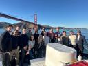 A group of coworkers pose on a boat in front of San Francisco's iconic Golden Gate Bridge