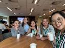 Five women in a Salesforce office sit at a table with coffee cups