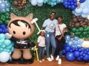 A woman and two younger children stand in front of a multi-colored balloon arch, next to a large statue of Salesforce's Astro character.