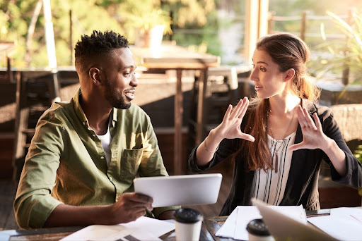 Two people sitting at a table consulting on a tablet.