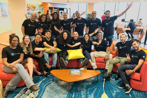 A group of Salesforce employees wearing Earthforce t-shirts are sitting on or standing around a bright orange couch, smiling for the camera