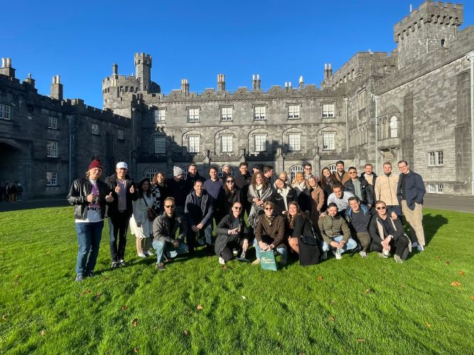 Kelsey and her team on a lush green lawn in front of the gray stone facade of Kilkenny Castle in Ireland.