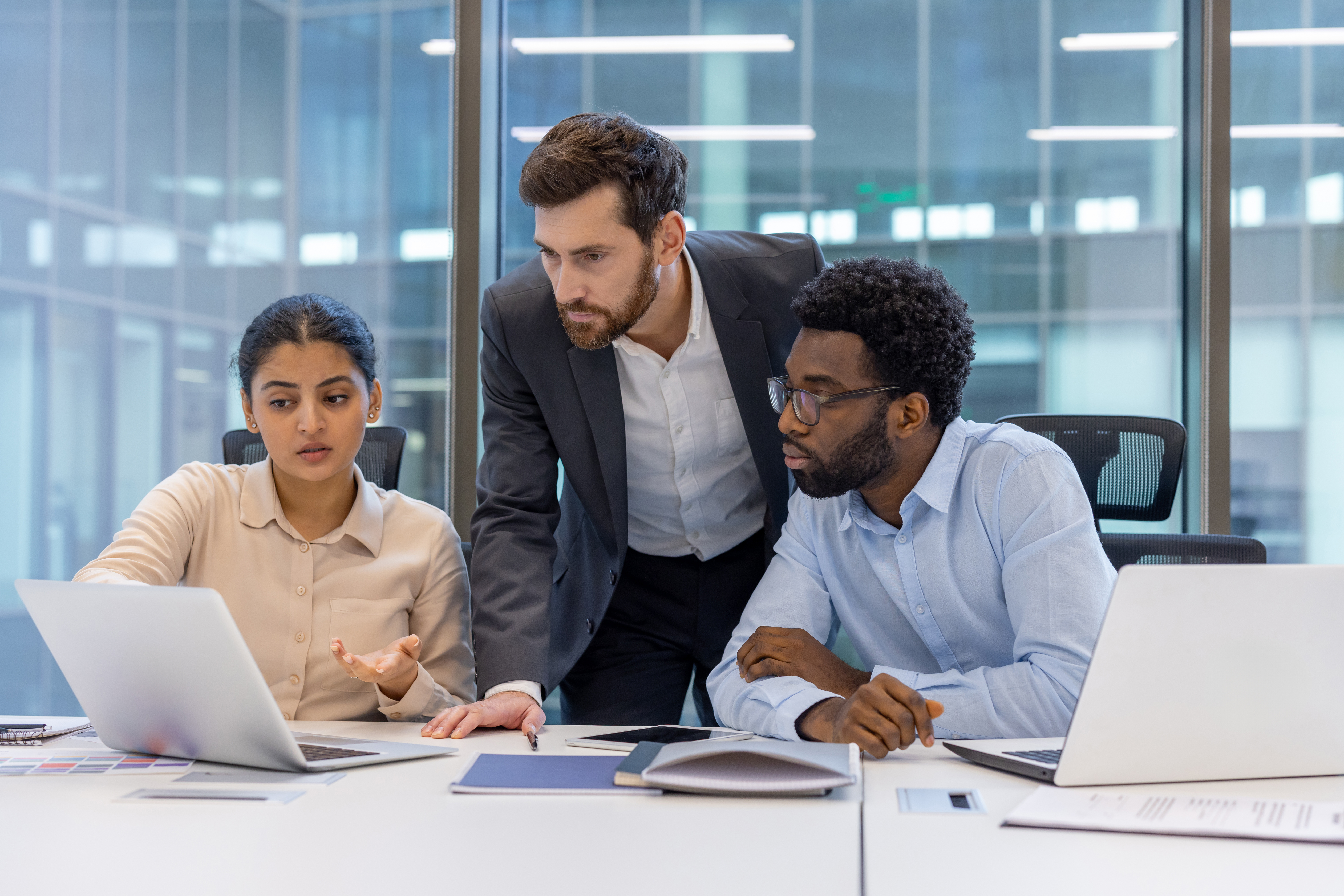 Group of professionals in a modern office discussing project strategy using laptops