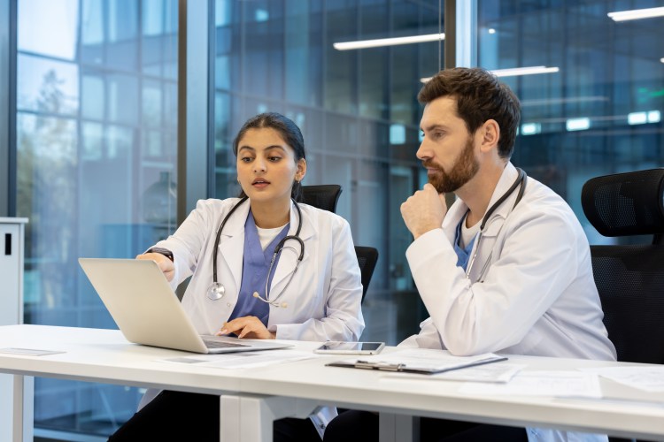 Two doctors, one female and one male, are looking at a laptop screen.
