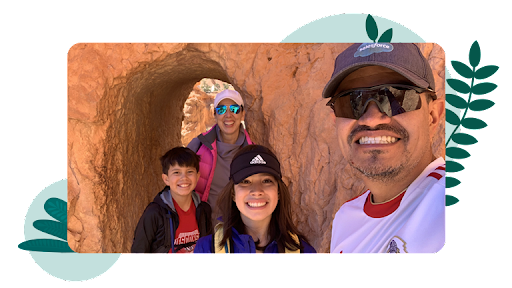 Carlos and his family on a hike take a photo under a natural red rock archway