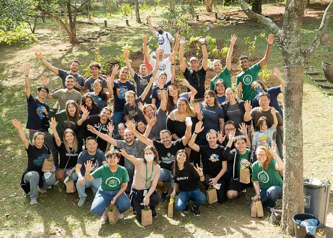 A group of Salesforce employees stand in a tree orchard and wave to the camera.