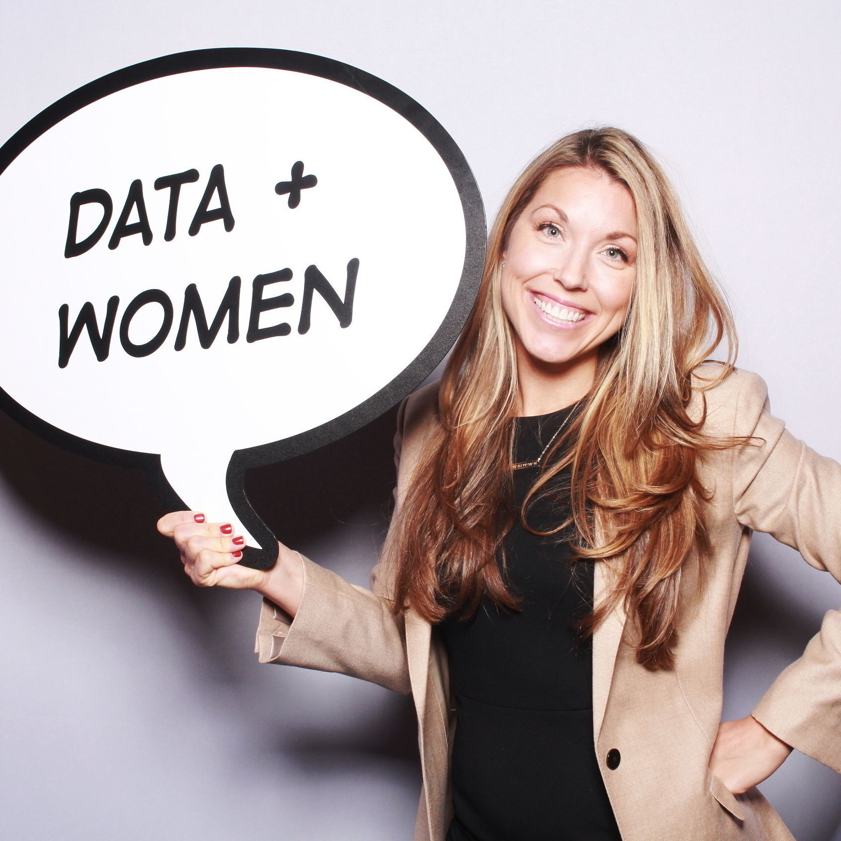 Sarah holds up a sign shaped like a speech bubble that says "DATA + WOMEN"