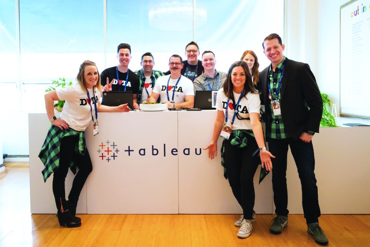A group of Tableau employees surround a table with the Tableau logo on it.
