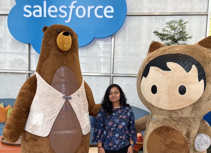 Nandini poses between Salesforce mascots Codey and Astro