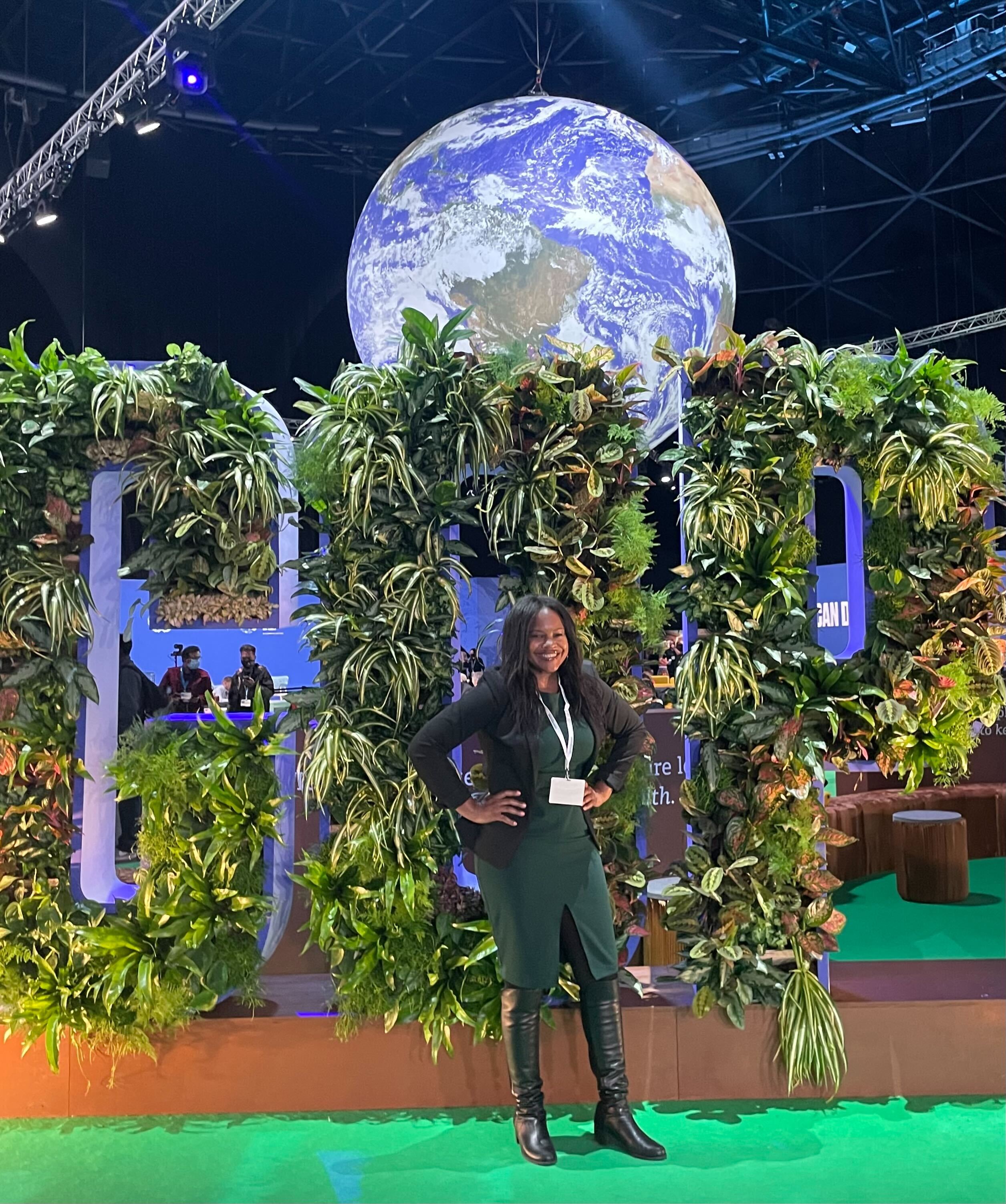 Bianca stands in front of a UN Climate Change Conference display of the letters "CDP" created out of plants, a giant earth globe in the background.