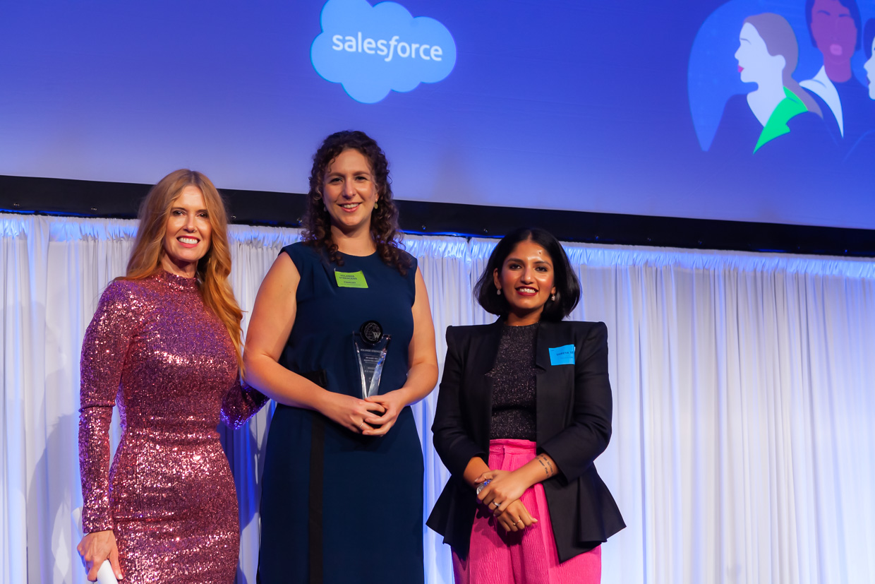 Shreya stands on a stage with two other colleagues, accepting an award.