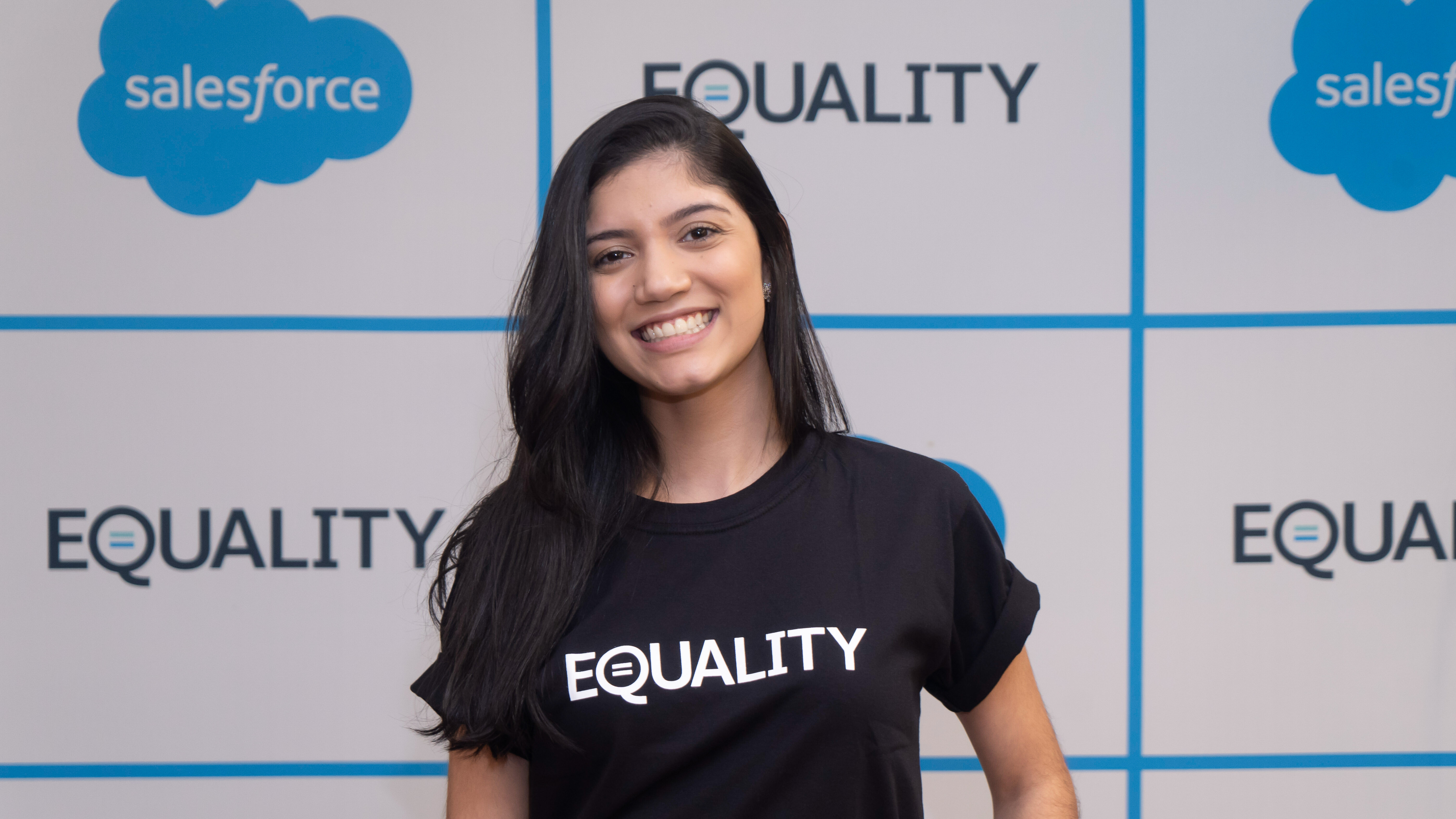 Beatriz wearing an Equality t-shirt in front of a step-and-repeat with Salesforce's logo and "Equality"