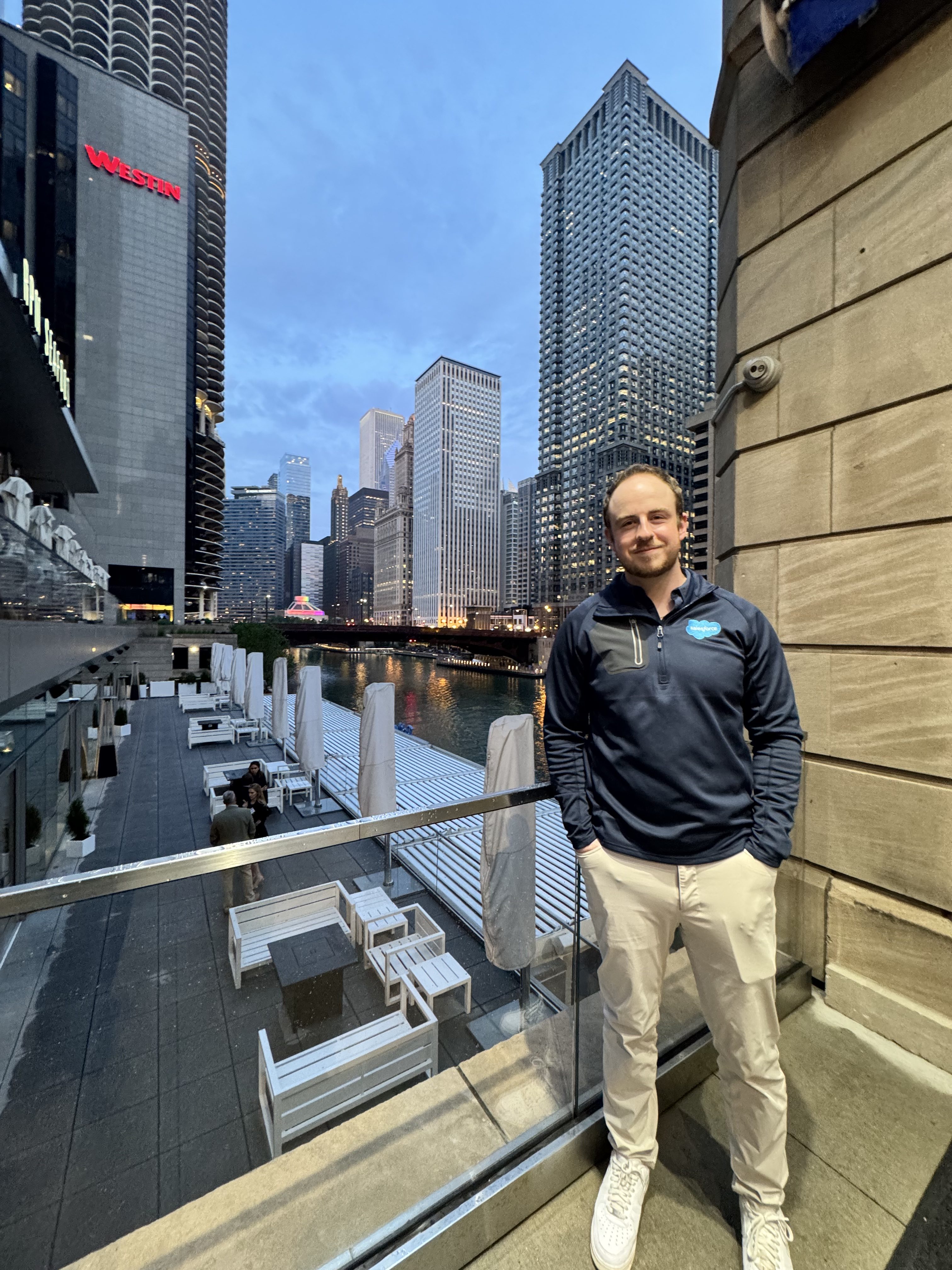 Samuel, wearing a Salesforce jacket, poses in front of the Chicago skyline at dusk