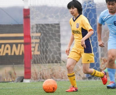 Mai playing soccer in a yellow and blue uniform