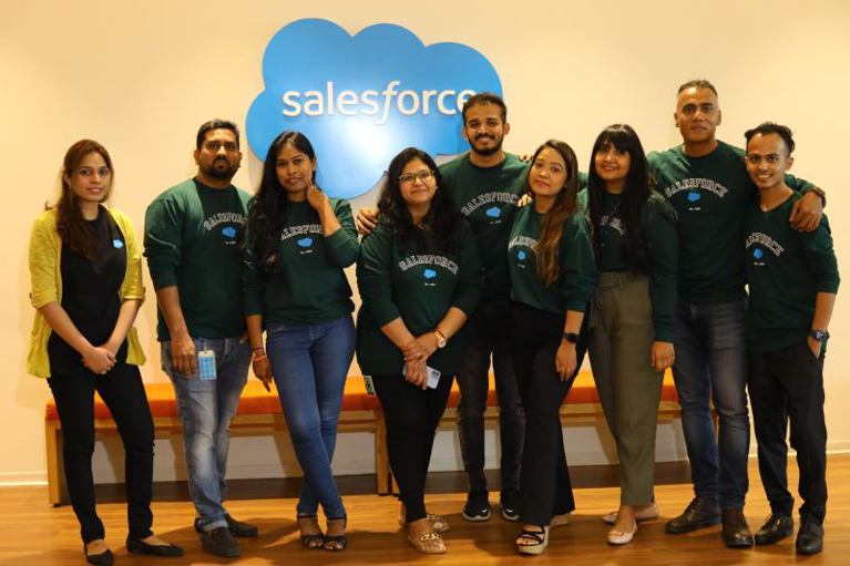 Sumit with his Futureforce team wear green Futureforce jumpers and stand in front of the Salesforce logo