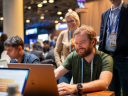 A man types on a laptop at Dreamforce while others look on.